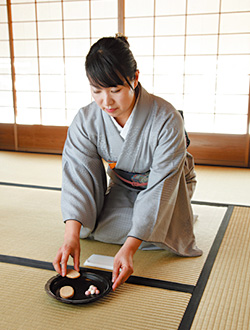 菓子器に左手を添えて菓子を1種類ずつ懐紙の上に取り、指先を懐紙の端で拭きます。