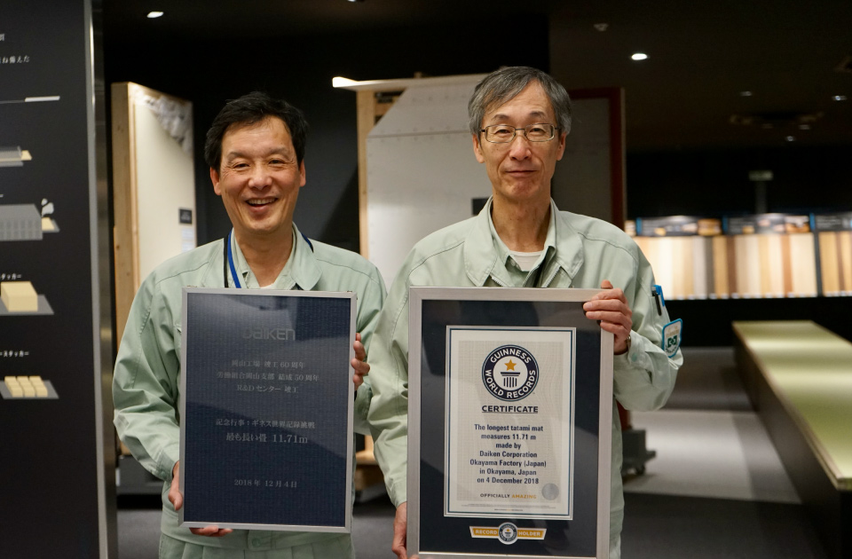 「最も長い畳／Longest tatami mat」のギネス世界記録の公式認定証を手にする岡山工場工場長の鳥羽亨二さん（右）と、（株）ダイタック代表取締役社長の長野智美さん（左）。