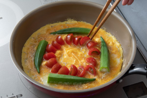 写真:フライパンに溶き卵を入れ、野菜を並べる