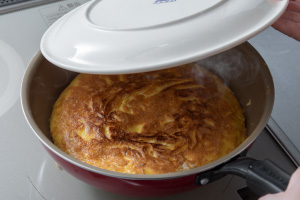 写真:フライパンに大きな皿をかぶせようとする