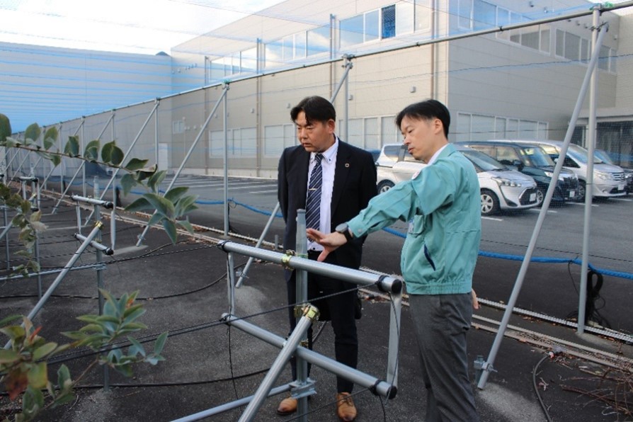 室谷社長（右）から工場敷地内で栽培しているブルーベリーについて説明を受ける中川地方参事官（左）